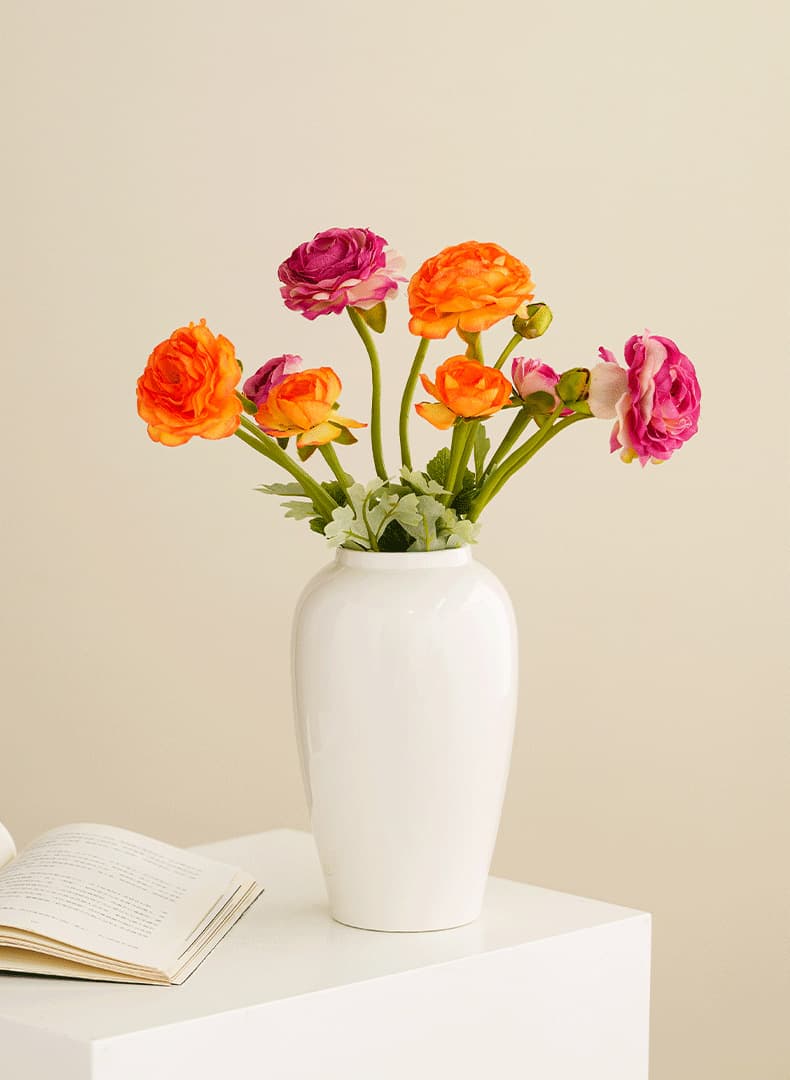 Minimalist white ceramic vase with colorful flowers on a white pedestal