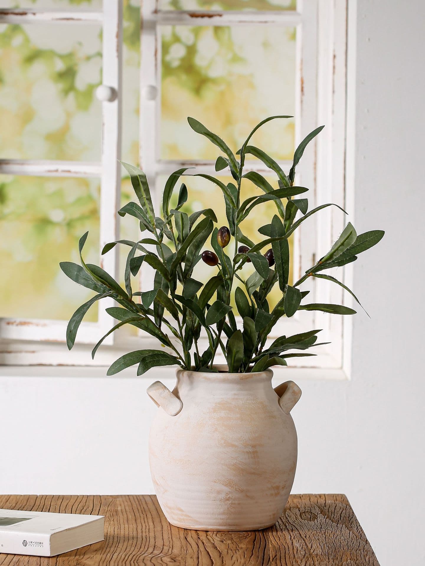 Retro handmade ceramic vase with leafy stems by a window