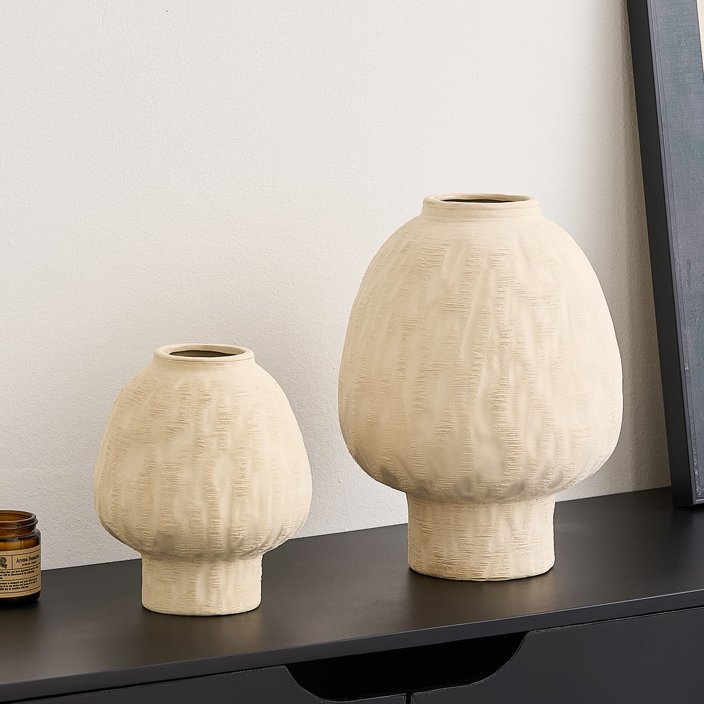Two ivory ceramic vases displayed together on a dark shelf