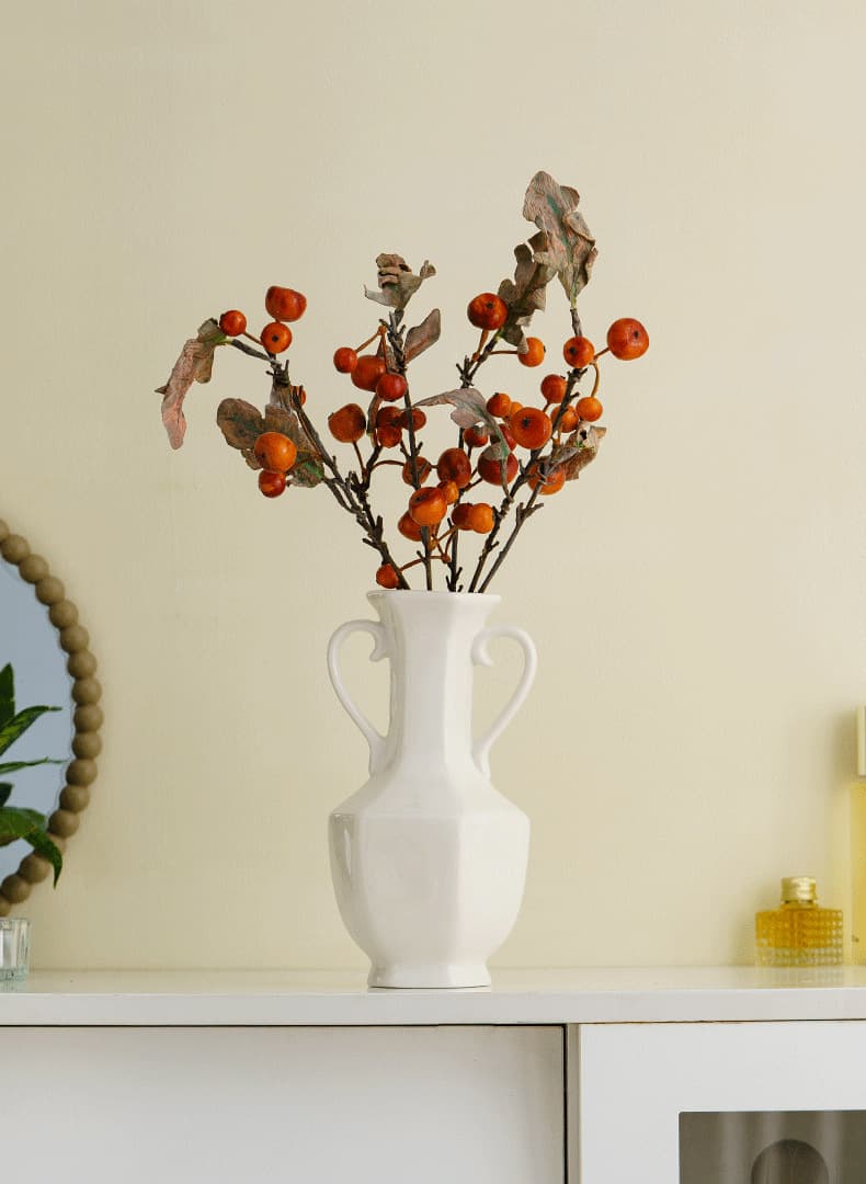 White ceramic hydroponic vase with autumn branches on a shelf