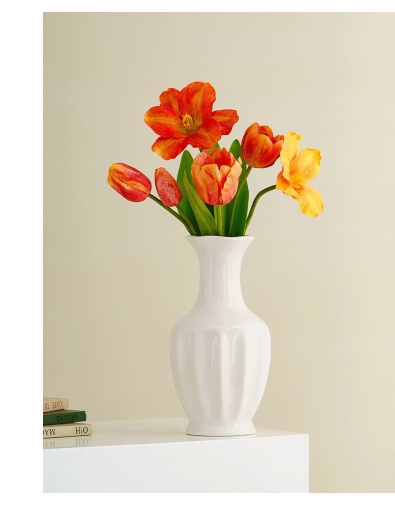 White ceramic hydroponic vase with orange flowers near a window