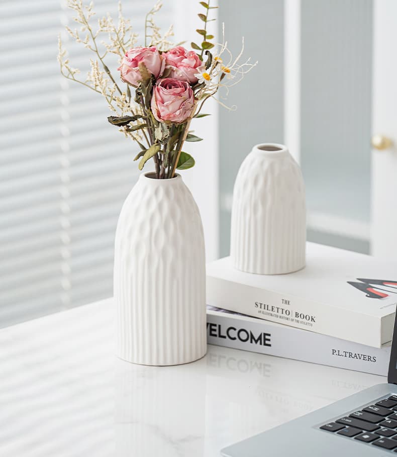 White ribbed ceramic vase styled beside a laptop and flowers
