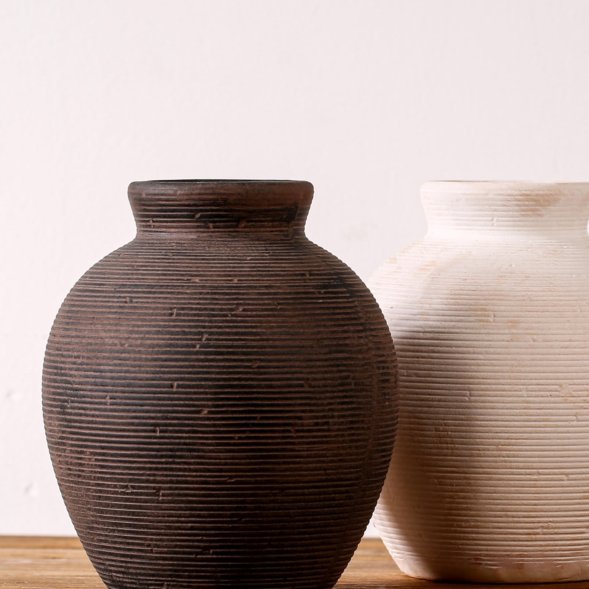 Dark clay textured ceramic vase detail beside cream vases